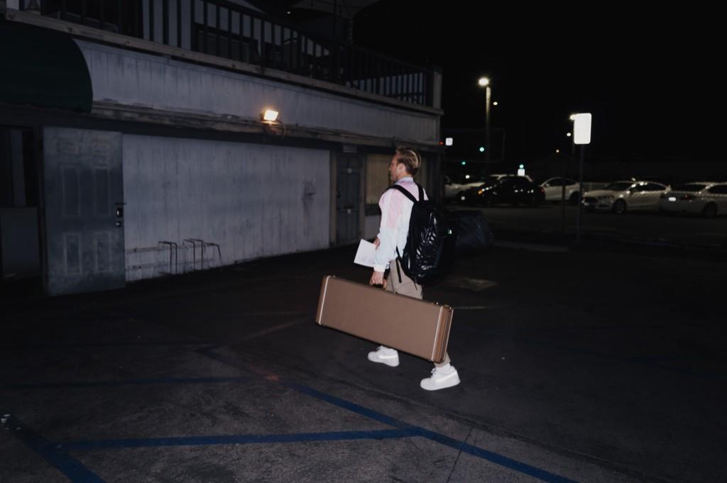 Luke Lively walking through a parking lot at night with guitar case and gear